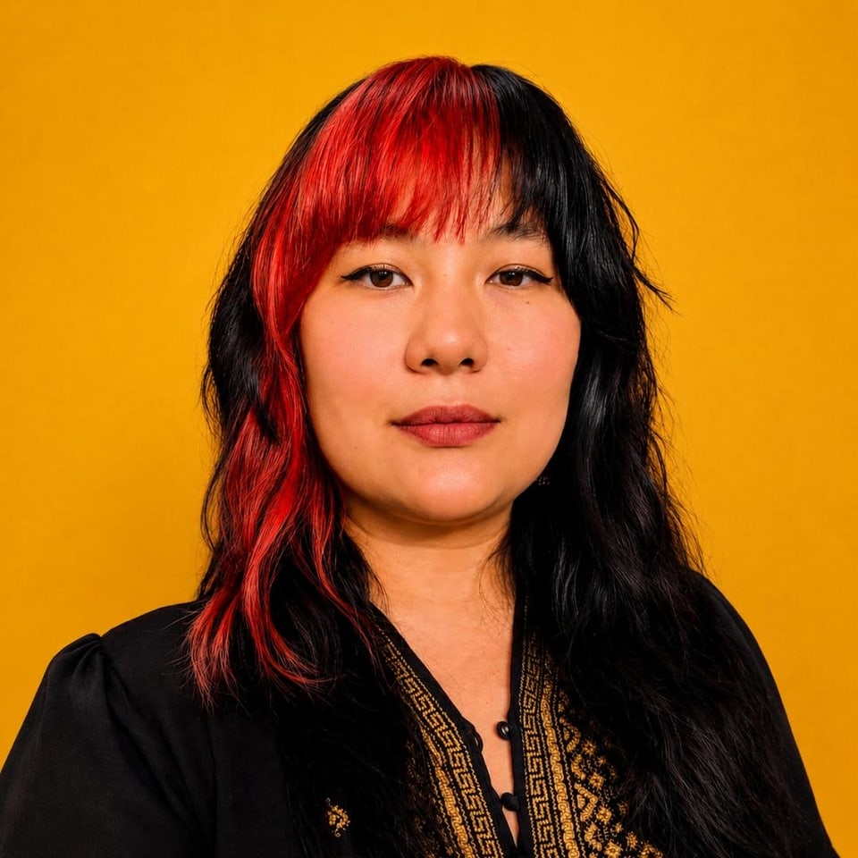 Portrait of Ngân with black and red hair against a golden-yellow background.